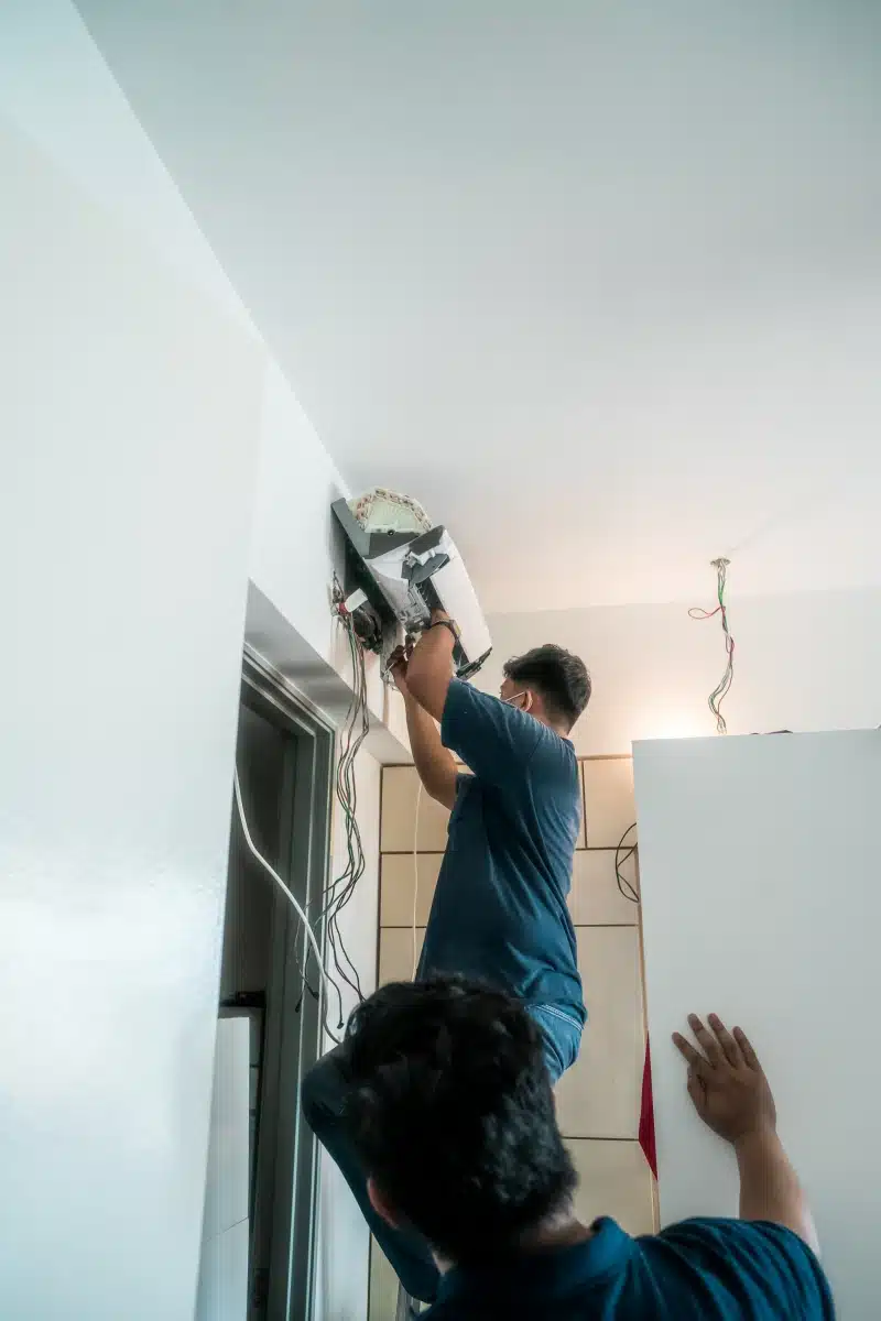 Dos instaladores colocando aire acondicionado split en Medellín, con cableado visible, trabajo en altura en espacio residencial.
